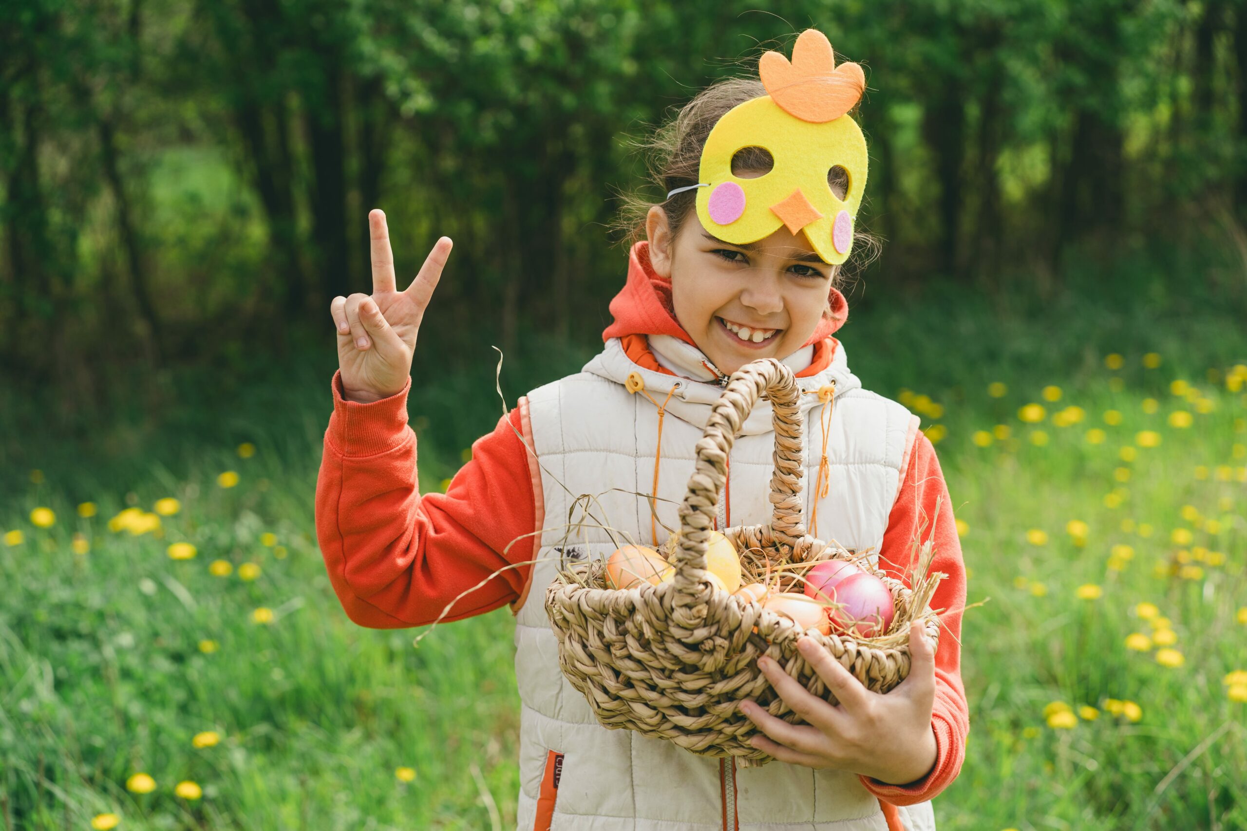 Funny girl with eggs basket and with a chicken mask on Easter egg hunt in sunny spring garden. Hunting for Easter eggs